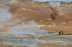 Volcanic area that houses a hot spring lake that is being photographed by several people.