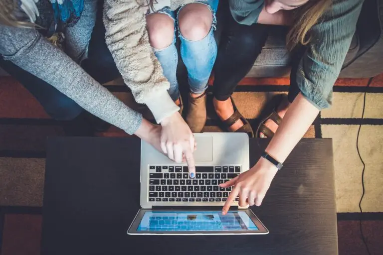 A top-down shot of a group of three people sitting in front of a laptop. They're pointing at a point on the screen.